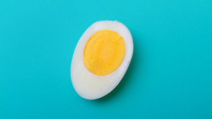A chicken egg cut in half with a round yolk on a blue background.