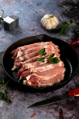 Raw pork meat slices with spices and herbs in a black pan. Black background. Top view space for text