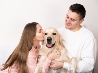 Happy family hugs the dog. A funny golden retriever in the arms of the owner. Husband and wife kiss and hug a pet