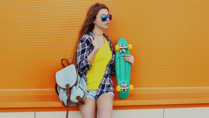 Portrait of young woman with green skateboard on a colorful orange background