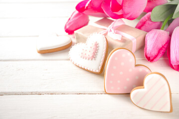 Valentine Day concept, Spring Woman Day Holiday, Mothers Day background, Red tulip flowers bouquet, craft paper gift box, heart shaped traditional sugar cookies, White wooden background copy space