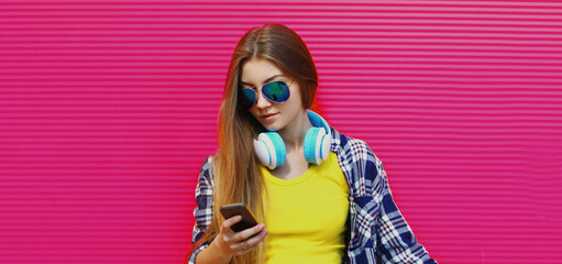 Portrait of young woman in wireless headphones with phone listening to music on a pink background