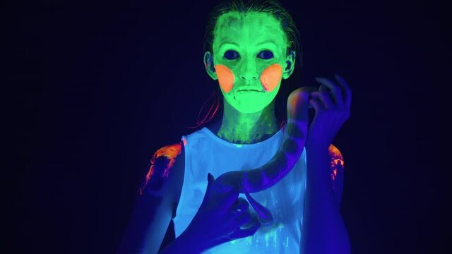 Video of woman with scary painted face in ultraviolet light holding snake