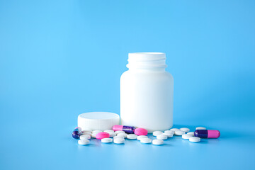 White plastic pill bottle with teblets pills on blue background with selective focus