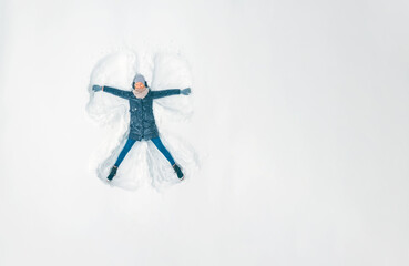 Young beautiful woman in a gray jacket, hat and gloves, blue jeans, boots makes a snow angel in the...