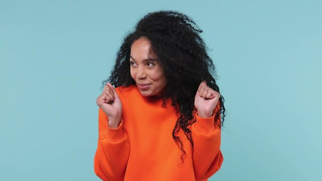 Fun confused shy shamed young african woman curly hair 20s years old in orange sweatshirt look camera spreading hands say oops i am so sorry isolated on pastel blue color background studio portrait
