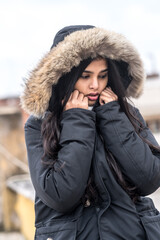 Cute young woman freezing in winter coat standing in street