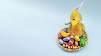 Toy chick and chocolate easter eggs on blue background with copy space