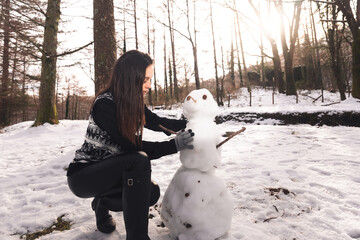 Young girl building a snowman on a snowy forest.