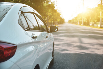 white car parked along the road against a natural backdrop with bright sunlight, focal point on the passenger door handle.