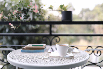 White coffee cup and notebooks on vintage metal table at balcony