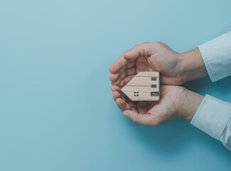 Businessman holding wooden house model on blue background , Protect house and asset concept.