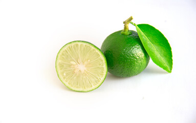 Whole green Thai lime with leaves and cut in half zig zag on white background.