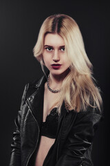 Fototapeta premium A beautiful, glamour young blond Girl dressed in a black jacket is posing on black background