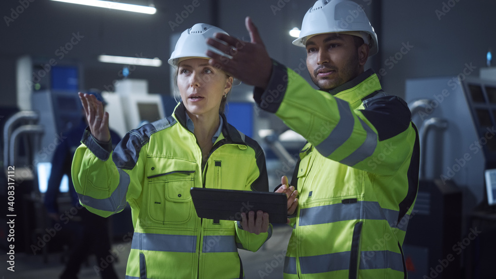 Poster Chief Engineer and Project Manager Wearing Safety Vests and Hard Hats, Use Digital Tablet Computer in Modern Factory, Talking, Optimizing Production Line. Industrial Facility with CNC Machinery