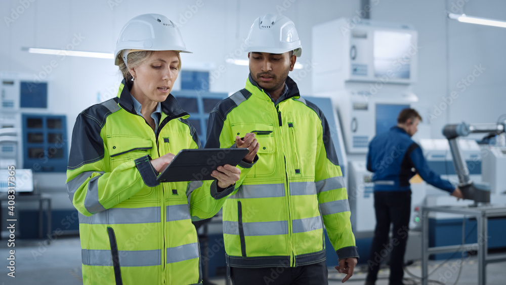 Poster chief engineer and project supervisor in safety vests and hard hats walk through modern factory, tal