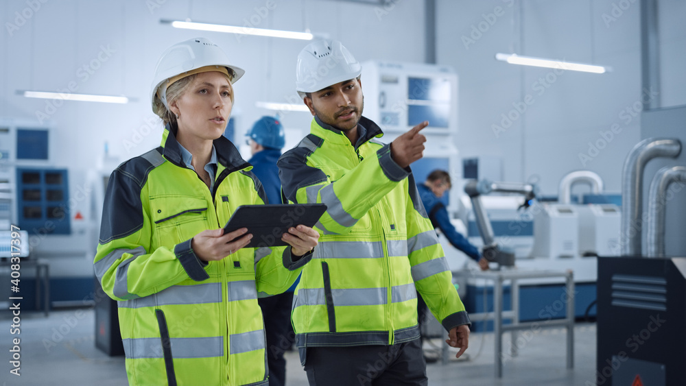 Poster chief engineer and project supervisor in safety vests and hard hats walk through modern factory, tal