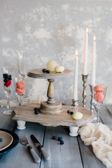Candles on a cake stand with a wooden background. Table with glasses, plate, burning candles and cutlery. Elegant festive table setting and room decor.