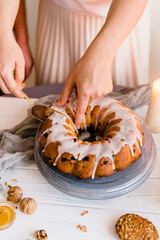Female hands ready to cut Freshly baked raisin sponge cake covered with glaze, served on a cooling tray with ingredients.