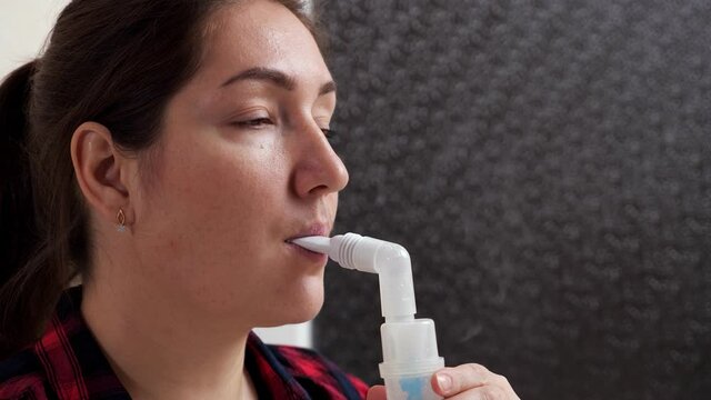 Close-up of woman inhaling steam using oral tube nebulizer.