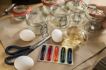 Frau mit Essig, Wasser und bunten Ostereier Kaltfarben in Rot, Orange, Gelb, Blau, Grün in Verpackung auf Papier Unterlage mit Gläser, gekochte Eier und Schere zum Färben zu Ostern