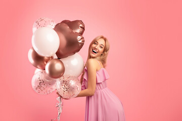 Carefree young lady with holiday balloons partying, celebrating birthday or anniversary over pink...
