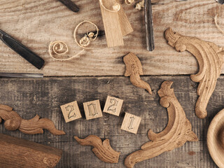 Wooden blcoks with Year 2021 and carved oak decorative elements on a rustic workbench with chisels