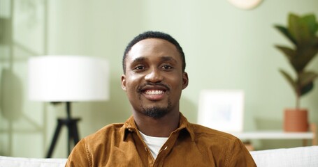 Close up portrait of happy african american young man at home, raising head looking at camera smiling on home decor background.