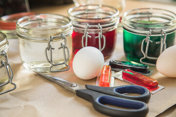 Bunte Ostereier Kaltfarben in Rot, Orange, Gelb, Blau, Grün in Verpackung auf Papier Unterlage mit Eier, Essig, Wasser, Gläser und Schere zum Färben zu Ostern