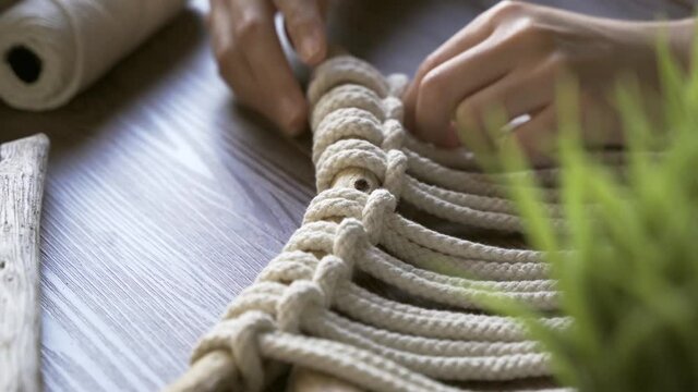 young woman hands checking over knots of macrame decoration in wooden table