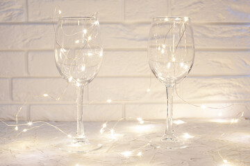 against the white brick wall two wine glasses, around the glasses a glowing garland
