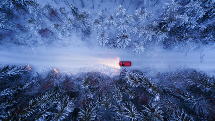 A red car rides along a winter road in the night forest. Snow on trees and roadsides, Aerial View. - 408321578