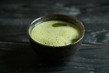 Japanese organic matcha green tea in bowl with chashaku spoon and chasen bamboo whisk on black wooden background. Healthy product from the nature typical of the Japanese tradition. Tea ceremony concep