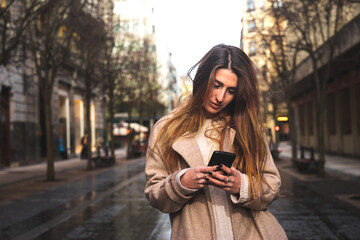 Obraz premium Young caucasian brunette woman using a smartphone at the street