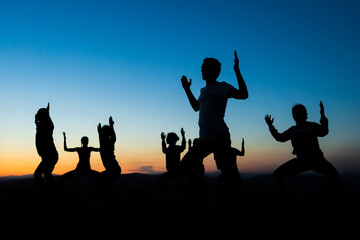 A group of silhouettes of people doing stretching and toning exercises after the running session or during a yoga class somewhere outdoors at sunset. Healthy living in a healthy body.