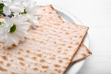 Plate with Jewish flatbread matza for Passover and flowers on white background, closeup