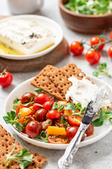 Tasty and healthy breakfast or lunch. Salad of colorful cherry tomatoes, onions, herbs, and olive oil, served with crispbread and feta cheese.