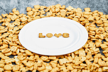 Scattered alphabet crackers and word love spelled with crackers on a white plate