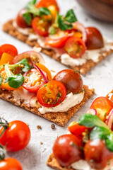 Crispbreads with feta cheese, colorful cherry tomatoes, onions, and herbs close-up. Toast with cream cheese and tomatoes on a gray background. Tasty breakfast or snack.