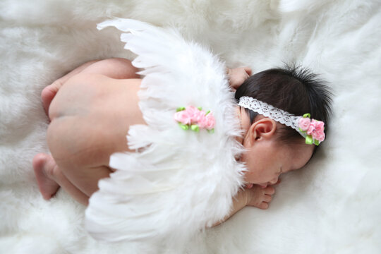 A beautiful newborn girl wearing a headband and small angle wing sleeping on a white soft blanket, Infant, babyhood concept and copy space - Image