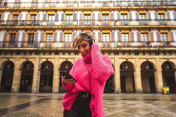 Young caucasian blonde woman listening music with headphones at the street