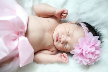 Obraz na płótnie Canvas A beautiful newborn girl wearing a pink headband and sleeping on a white soft blanket, Infant, babyhood concept and copy space - Image