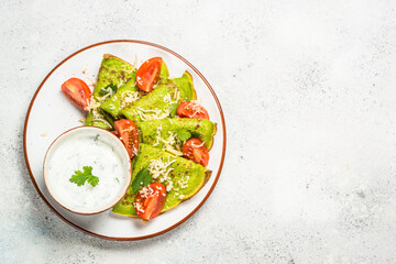 Green pancakes from spinach with cheese and tomatoes and yogurt sauce at white table. Top view with copy space.