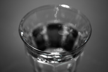 Top of a drinking glass filled with fresh water against a dark background. Focus on the edge in front