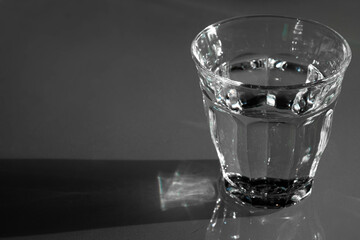Drinking glass filled with fresh water on a a dark table. Focus on the edge in front. Shadow to the left