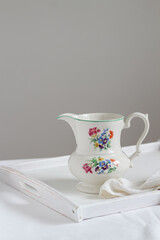 White vintage pitcher decorated with tiny flowers on a white tray. Minimalistic cottage style still life