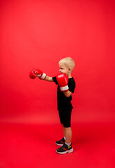 a little boy boxer stands sideways and makes a punch in boxing gloves on a red background with space for text