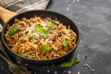 Pasta Bolognese, meat ragout in tomato sauce in the skillet at black table. Italian cuisine.