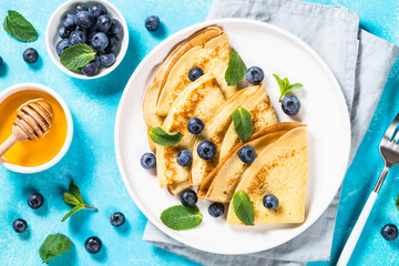 Crepes with blueberries and honey at blue table. Healthy breakfast or snack. Top view with copy...