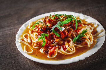 Sliced fried meat with vegetables and mushrooms in a sauce with bavette pasta in a plate on wooden table